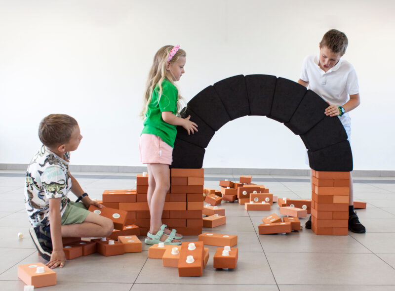 Trójka dzieci buduje łuk z cegieł podczas warsztatów Konstrukcje z cegieł i stali w Kopalni Ignacy.