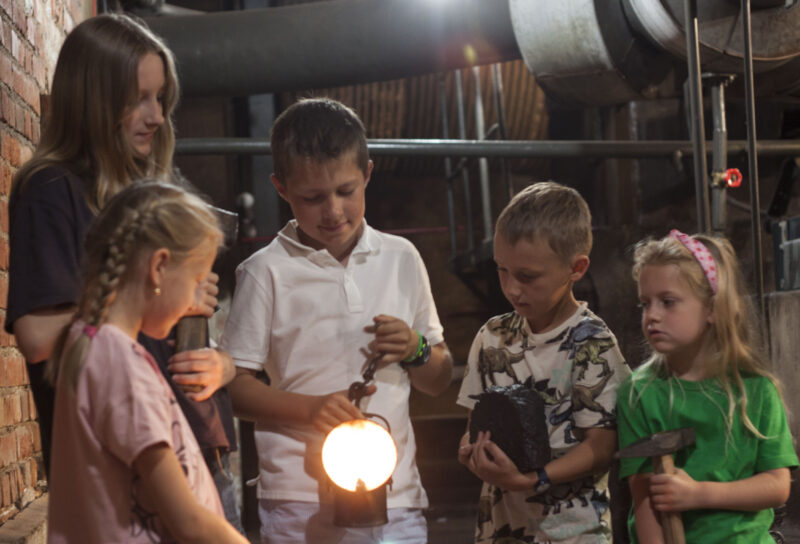Dzieci w murach Kopalni Ignacy trzymają lampę i obserwują, jak działa, podczas warsztatów Światło w tunelu.